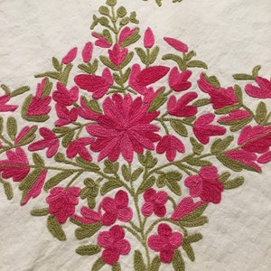 May include: White fabric with pink and green embroidered floral design. The embroidery features a large pink flower with smaller pink flowers and green leaves.