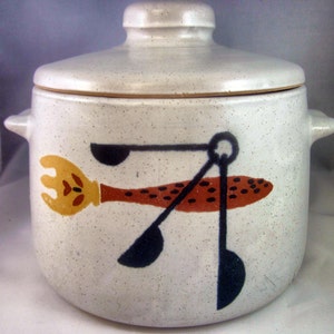 May include: White ceramic crock pot with a lid. The crock pot has a brown and black design of a fish with three spoons attached to it.
