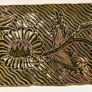 May include: A wooden batik stamp with a floral design. The stamp is carved with intricate details of flowers and leaves. The background of the stamp is a wavy pattern.