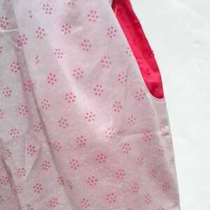 May include: A white fabric with a pink polka dot pattern. The fabric has a pink seam on the right side.