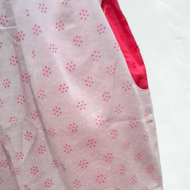 May include: A white fabric with a pink polka dot pattern. The fabric has a pink seam on the right side.