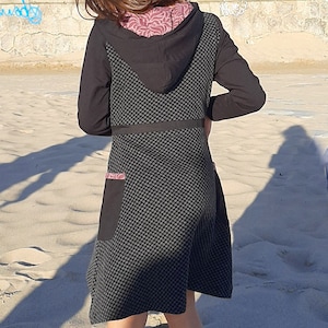 May include: A black hooded dress with a geometric pattern and a pink trim. The dress has a pocket on the side and a black belt.