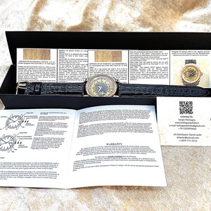May include: A luxury wristwatch with a black leather strap and a gold-toned face, displayed in a black box. The watch is accompanied by documentation and a warranty card. The watch strap is approximately 22 cm long.