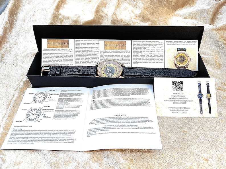 May include: A luxury wristwatch with a black leather strap and a gold-toned face, displayed in a black box. The watch is accompanied by documentation and a warranty card. The watch strap is approximately 22 cm long.