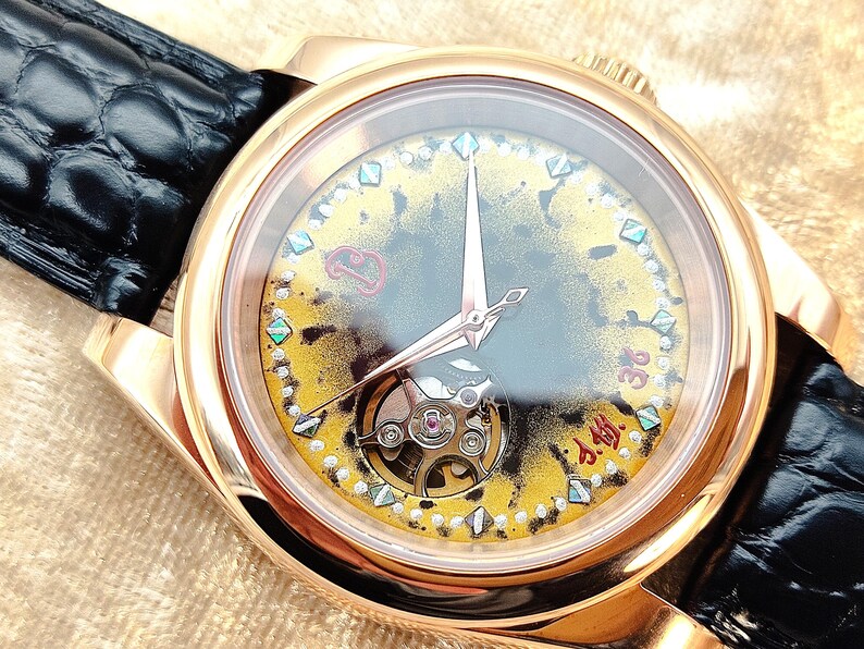 May include: A gold-coloured wristwatch with a black leather strap. The watch face has an intricate design with a visible mechanism, gold and yellow accents, and diamond-shaped markers. The hands are rose-gold coloured.