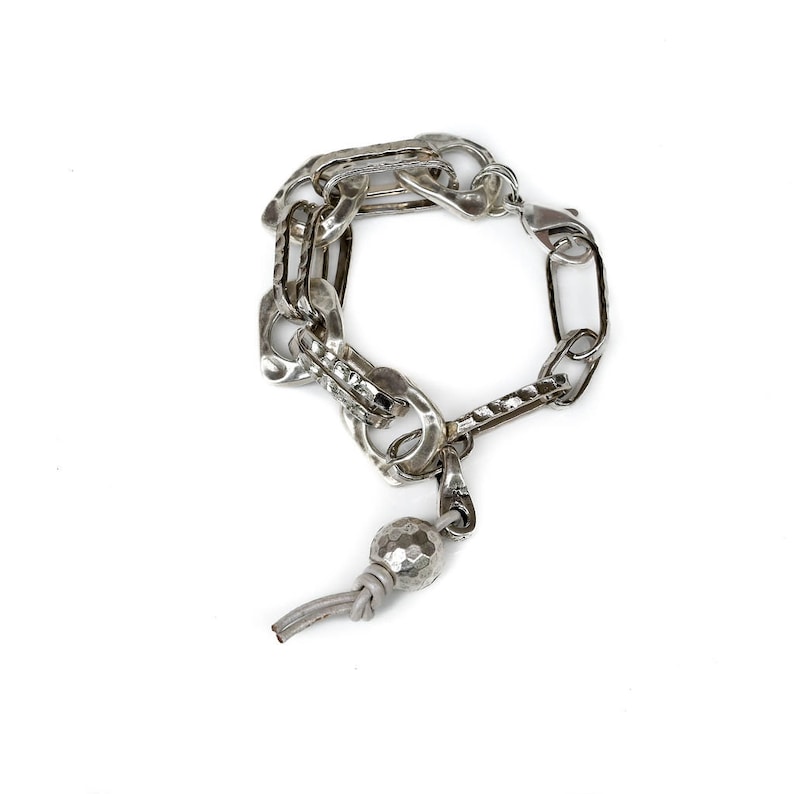 May include: A silver chain bracelet with a textured silver bead charm. The bracelet is made of multiple chain links of different sizes and styles.