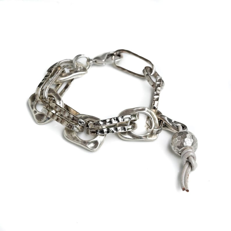 May include: A silver bracelet with a chunky chain design and a small silver bead with a grey leather tassel.