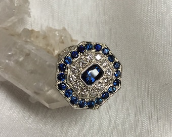 May include: Octagonal ring with a large blue sapphire surrounded by smaller blue sapphires and white diamonds.