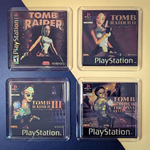 May include: Four clear plastic coasters featuring images from the Tomb Raider video game series. The coasters display the game titles and the PlayStation logo. The first coaster shows the original Tomb Raider, the second shows Tomb Raider II, the third shows Tomb Raider III, and the fourth shows Tomb Raider: The Last Revelation.