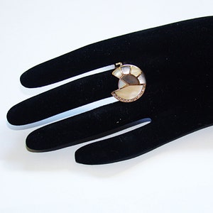 May include: A gold ring with a large, white, and gray, semi-circular stone set in the center. The stone is made of multiple pieces of mother of pearl.