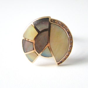 May include: A gold ring with a semi-circular design featuring a mosaic of iridescent mother-of-pearl pieces. The ring is accented with a row of small diamonds around the edge.