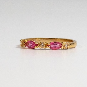 May include: A gold band ring with three pink oval-shaped gemstones and smaller clear gemstones set in the band.