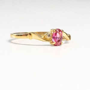 May include: A gold ring with a pink oval gemstone and two smaller white gemstones. The ring has a delicate, twisted band.