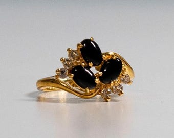 May include: A gold ring with a cluster of black oval gemstones and smaller clear stones. The ring has a wavy band.