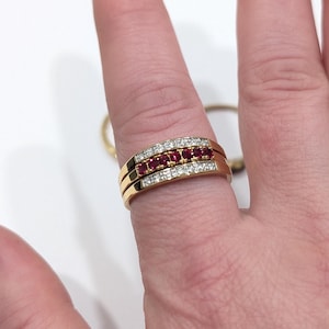 May include: A gold ring with a row of red gemstones and a row of white gemstones. The ring is on a finger, with a plain gold band visible behind it.