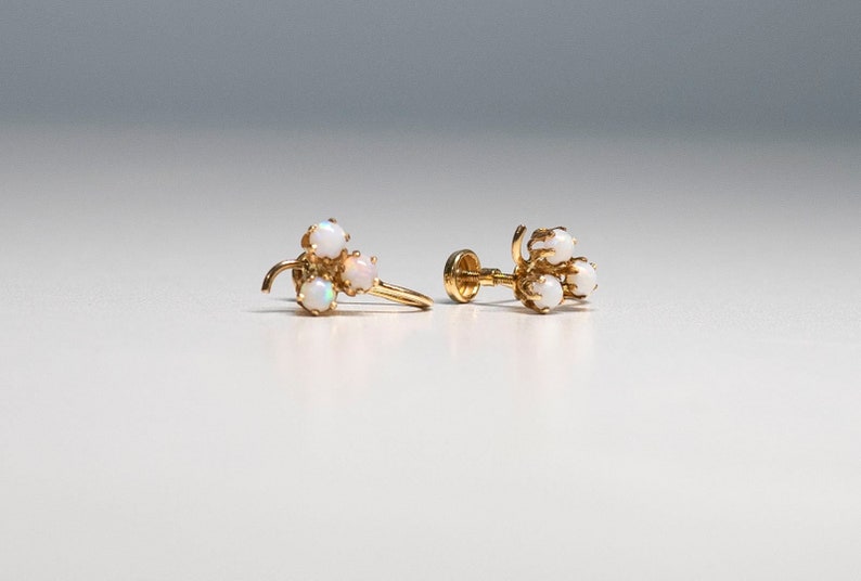 Op de afbeelding: Een paar gouden oorbellen met een cluster van drie witte opalen aan elke oorbel.