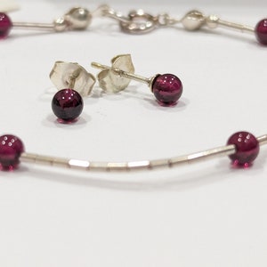 May include: A silver bracelet with five dark red gemstone beads and matching stud earrings. The bracelet is made of small silver beads.