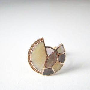 May include: A gold ring with a semi-circular design featuring a mosaic of mother-of-pearl and small clear stones.