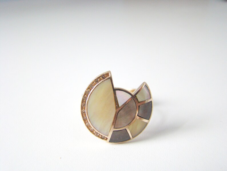 May include: A gold ring with a semi-circular design featuring a mosaic of mother-of-pearl and small clear stones.