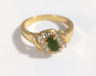 May include: A gold ring with a green oval gemstone surrounded by clear rhinestones.
