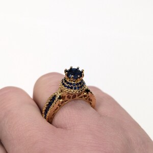 Peut inclure: Une bague en or avec une grande pierre pr&eacute;cieuse bleue entour&eacute;e de plus petites pierres bleues. La bague a un design d&eacute;licat et complexe.
