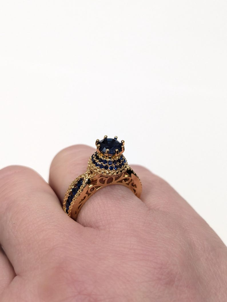 Peut inclure: Une bague en or avec une grande pierre pr&eacute;cieuse bleue entour&eacute;e de plus petites pierres bleues. La bague a un design d&eacute;licat et complexe.