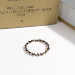 May include: A thin ring featuring a twisted design with alternating strands of gold-filled and sterling silver metal. The packaging text reads PRECIOUS BRAID GOLD-FILLED and STERLING SILVER RING 6.