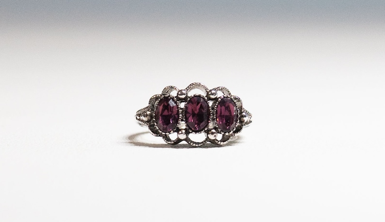 May include: A silver ring with three oval-shaped purple gemstones set in a delicate filigree design.