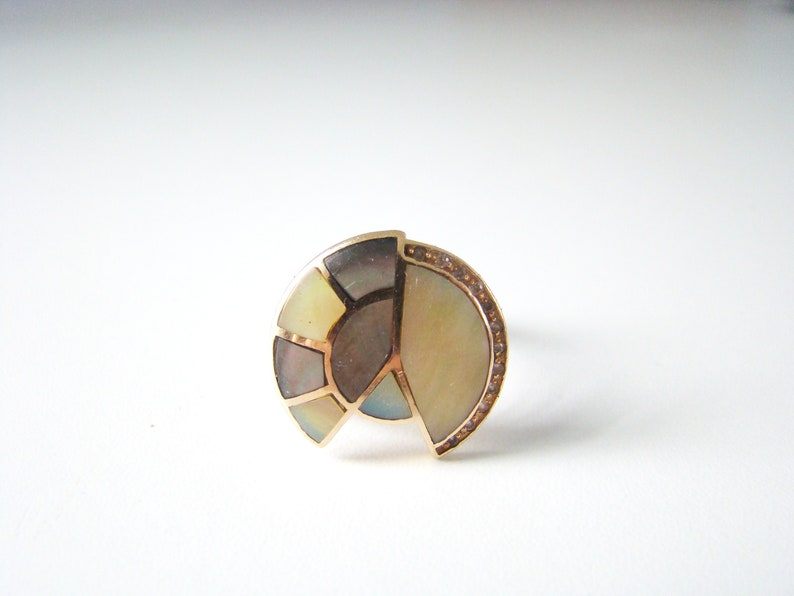 May include: A gold ring with a semi-circular design featuring a mosaic of iridescent mother-of-pearl pieces. The ring is accented with a row of small diamonds around the edge.