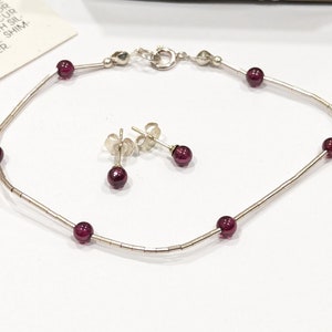 May include: A silver bracelet with a delicate chain and small red gemstones. Matching stud earrings with red gemstones are also included.