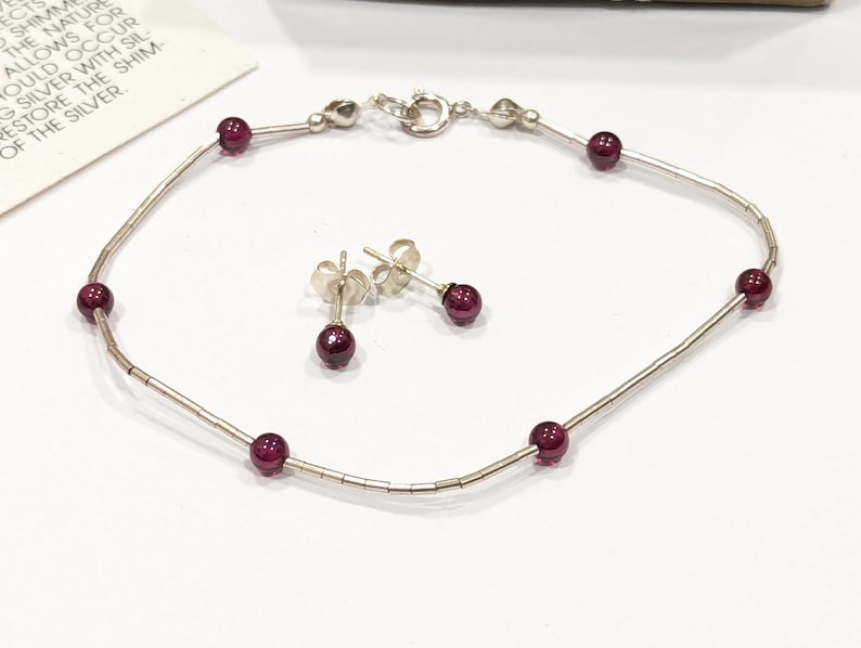 May include: A silver bracelet with a delicate chain and small red gemstones. Matching stud earrings with red gemstones are also included.