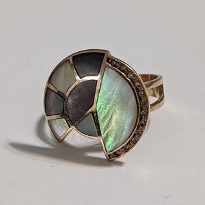May include: A gold ring with a large, multi-colored, iridescent, abalone shell design. The shell is set in a gold band and has a row of small diamonds around the edge.