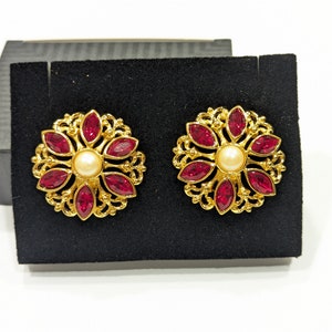May include: A pair of gold earrings with a floral design. Each earring features a central pearl surrounded by eight red gemstones.