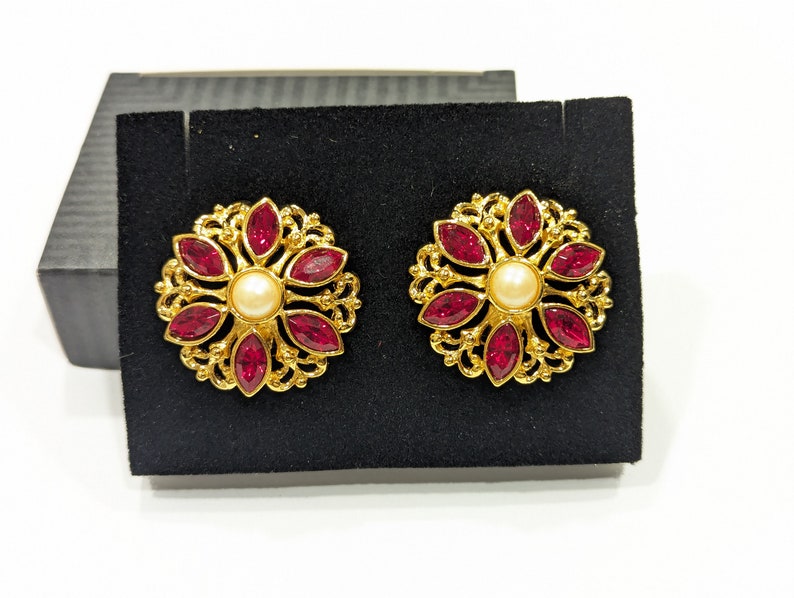 May include: A pair of gold earrings with a floral design. Each earring features a central pearl surrounded by eight red gemstones.