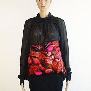 May include: A black sheer blouse with a long sleeve and a high neck. The blouse has a colorful, abstract design on the front, with pink, orange, and brown tones.
