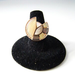 May include: A ring with a large, circular, multi-faceted gemstone set in gold. The gemstone is made of iridescent mother-of-pearl and has a geometric design.