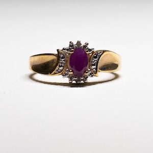 May include: A gold ring with a large, oval-shaped ruby surrounded by a halo of smaller diamonds.