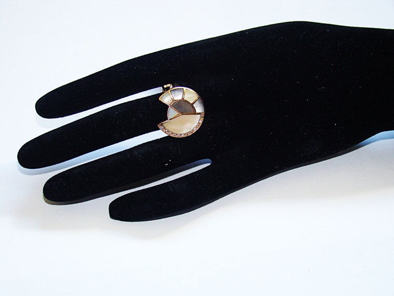 May include: A gold ring with a large, white, and gray, semi-circular stone set in the center. The stone is made of multiple pieces of mother of pearl.