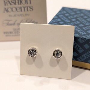 May include: A pair of silver stud earrings with clear crystal stones. The earrings are displayed on a white card with the text "Fashion Accents in Jewelry Touch of Class Pierced Earrings".