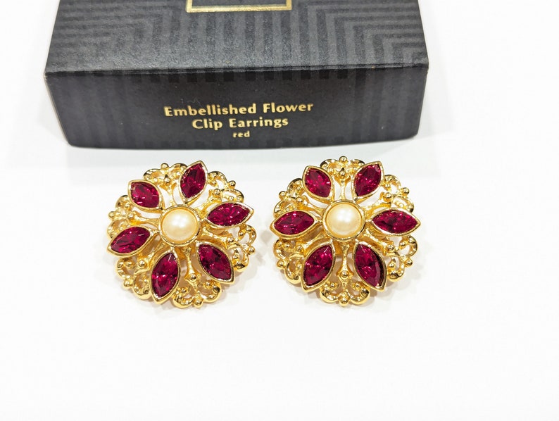 May include: A pair of gold clip-on earrings with a red flower design and a pearl center. The earrings are labeled "Embellished Flower Clip Earrings red".