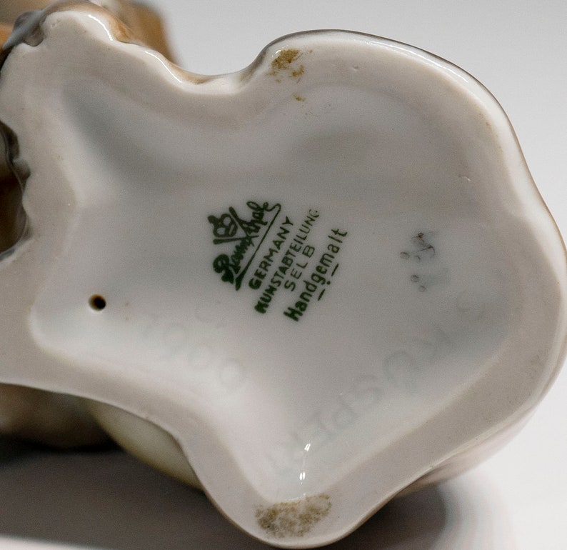 Może przedstawiać: Zbliżenie na sp&oacute;d porcelanowej figurki. Figurka jest oznaczona słowami "Germany, Kunstabteilung, Selb, Handgemalt" zielonym nadrukiem.