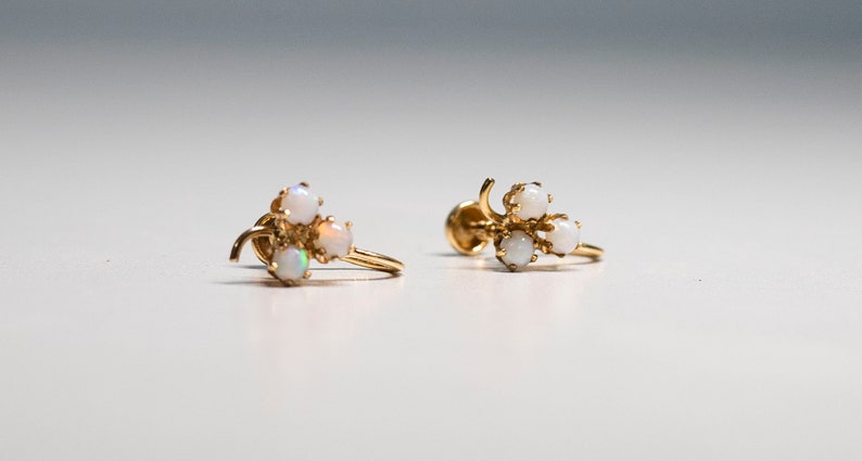 Op de afbeelding: Een paar gouden oorbellen met een cluster van vier witte opalen. De oorbellen zijn ontworpen in een delicate, bloemvormige vorm.