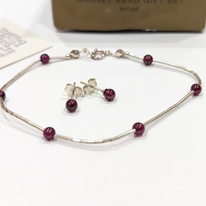 May include: A silver bracelet and earrings set with small, dark red garnet beads.