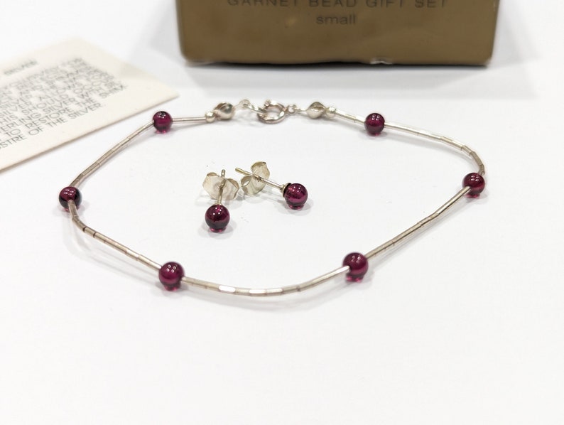 May include: A silver bracelet and earrings set with small, dark red garnet beads.