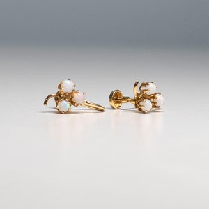 Op de afbeelding: Een paar gouden oorbellen met een cluster van drie witte opalen aan elke oorbel.