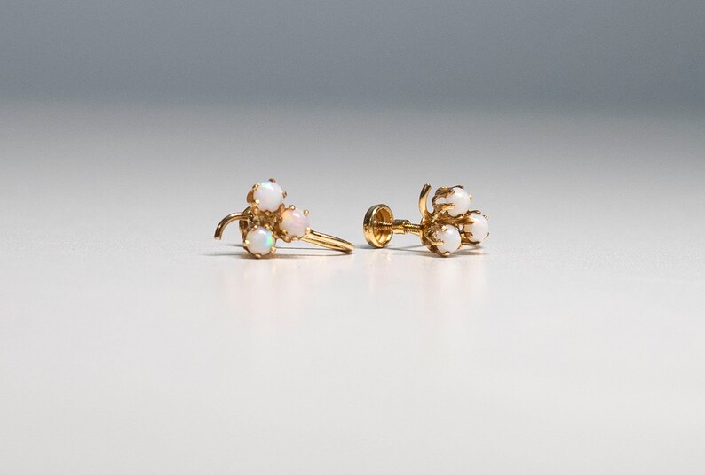 Op de afbeelding: Een paar gouden oorbellen met een cluster van drie witte opalen aan elke oorbel.