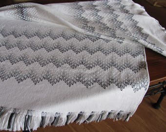 May include: White crocheted throw blanket with a black and white geometric pattern. The blanket has a fringe border.
