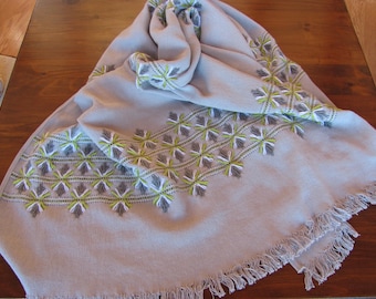 May include: A gray throw blanket with a fringe border and embroidered geometric patterns in white and green.