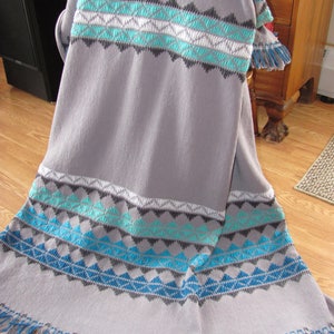May include: Gray throw blanket with a geometric pattern in shades of blue, teal, and white. The blanket has a fringe border.