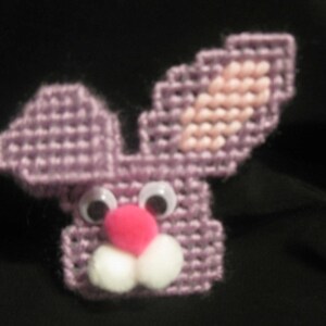 May include: A purple crocheted bunny with pink ears, white googly eyes, a pink pom-pom nose, and white felt teeth.